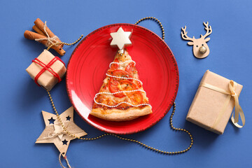 Plate with delicious pizza slice and Christmas decor on blue background