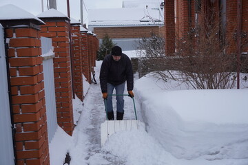 A man cleans snow in the winter in the courtyard of the house.