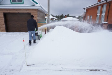 A man cleans snow in the winter in the courtyard of the house,  man cleaning snow with a snow blower