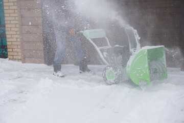 A man cleans snow in the winter in the courtyard of the house,  man cleaning snow with a snow blower