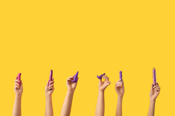 Female hands with different sex toys on yellow background - obrazy, fototapety, plakaty