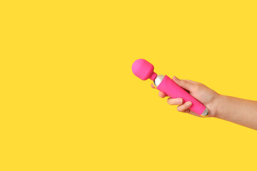 Female hand with pink vibrator on yellow background