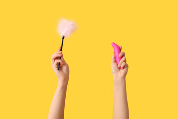 Female hands with sex toys on yellow background