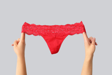 Female hands with sexy red panties on grey background, closeup - obrazy, fototapety, plakaty