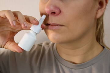 Close up of sick woman with red nose using a nose spray, blurry background