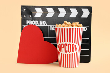 Movie clapper with bucket of popcorn and paper heart on yellow background. Valentine's Day...