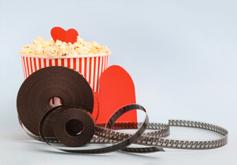 Bucket of popcorn with paper hearts and film reel on grey background. Valentine's Day celebration