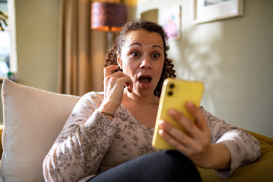 Surprised Woman Reacting to Smartphone Content While Sitting on Couch