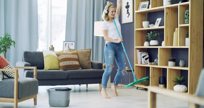 Cleaning, dancing and a woman with headphones for music in a house for fun energy and housework. Young female person in her apartment home with happiness, singing and joy to mop and clean floor
