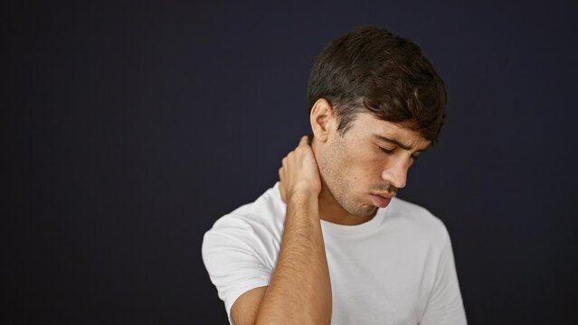 Handsome Young Hispanic Guy Suffering Serious Backache, Standing In Relaxed Concentration, Tired And Stressed Touching Injured Neck On Isolated Black Background, Portrait Looking Away From Camera