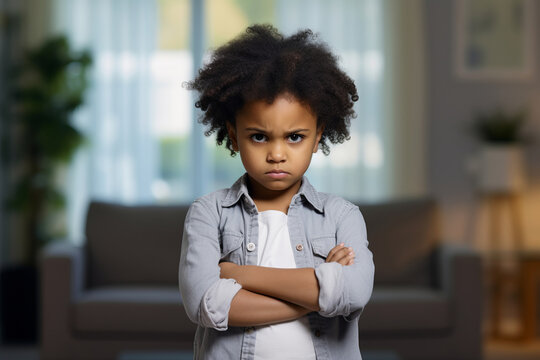 Angry annoyed child looking at the camera with it's hand crossed. Irritated displeased kid in a living room.