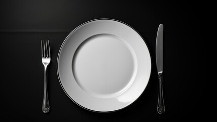 A minimalist dinner setting with a white plate and silver cutlery on a black background