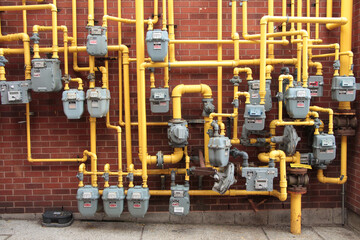 a lot bunch of gray enbridge gas meters bunched together mounted to brick wall with yellow gas pipes coming out of them