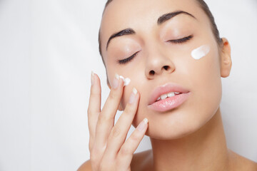 Obraz na płótnie Canvas beautiful model applying cosmetic cream treatment on her face white
