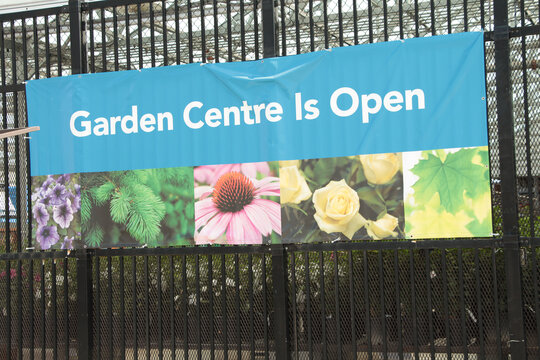 garden centre is open caption writing text sign with pictures of flowers and plants on a black fence, white and blue