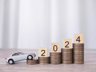 Wooden block with number 2024 on stack of coins and toy car. The concept of saving money for car loan, insurance, paying tax in new year 2024