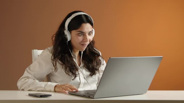 A beautiful girl in white headphones is watching a video on her laptop. She cheers enthusiastically and can't contain her joyful emotions. High quality 4k footage