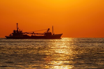夕日を浴びながらサンロードの上を進む貨物船の情景