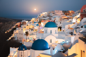 Seaside moonlit view at night of traditional white wash buildings and blue dome churches at the...