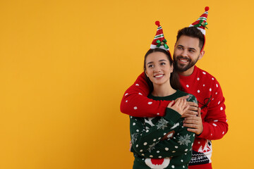 Happy young couple in Christmas sweaters on orange background. Space for text