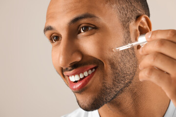 Handsome man applying cosmetic serum onto face on light grey background, closeup - Powered by Adobe