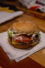 hamburguesa con queso, tomate y lechuga, sobre una servilleta blanca en un restaurante de comida rápida en vertical