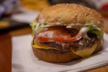 Toma cercana de una hamburguesa con queso, lechuga y tomate, sobre una servilleta blanca en un restaurante de comida rápida