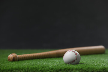 Baseball bat and ball on green grass against dark background. Space for text