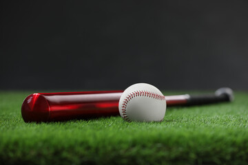 Baseball bat and ball on green grass against dark background. Space for text