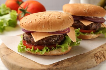 Tasty hamburgers with patties, cheese and vegetables on wooden board, closeup