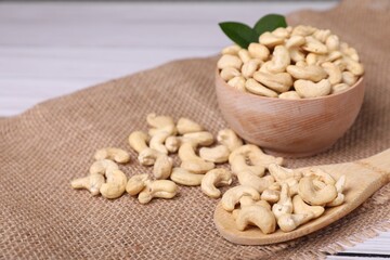 Tasty cashew nuts and green leaves on table, closeup. Space for text