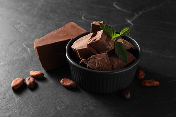 Pieces of tasty milk chocolate, mint and cocoa beans on black table
