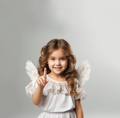 beautiful caucasian girl with angel wings and white dress smiles and points her finger upwards, concept of angel and cupid. white background