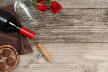 Fototapeta na wymiar Bottle of red wine, glass, chocolate truffles, corkscrew and roses on wooden table, flat lay. Space for text