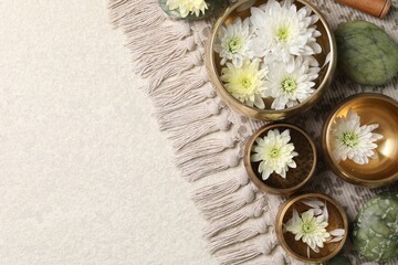 Tibetan singing bowls with water, beautiful chrysanthemum flowers and stones on table, flat lay. Space for text