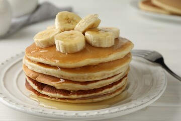 Fototapeta na wymiar Delicious pancakes with bananas and honey on white wooden table, closeup