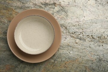 Beautiful beige ceramic plates on gray textured table, top view. Space for text