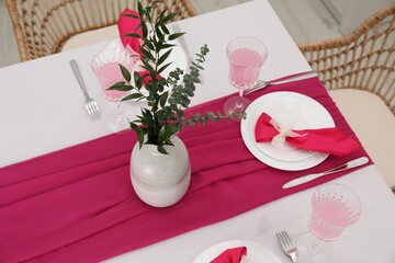 Table setting. Glasses of tasty beverage, plates, pink napkins and vase with green branches in dining room, above view