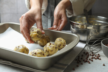 Woman putting raw chocolate chip cookie ball on baking pan at table, closeup