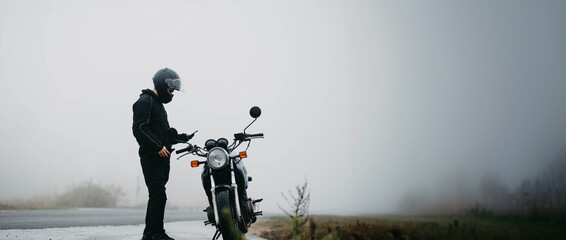 male motorcyclist with a motorcycle on a foggy asphalt road. - obrazy, fototapety, plakaty
