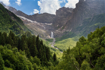Fototapeta na wymiar Waterfall flowing down from the mountain range and the Dzhuguturluchat glacier in the mountains of the North Caucasus near the village of Dombay on a sunny summer day, Karachay-Cherkessia, Russia