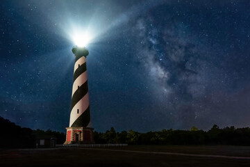 Historic Cape Hatteras Lighthouse shines brightly in a night sky full of stars and the galactic center of the Milky Way Galaxy at Cape Hatteras National Seashore on the Outer Banks of North Carolina. - 690466364