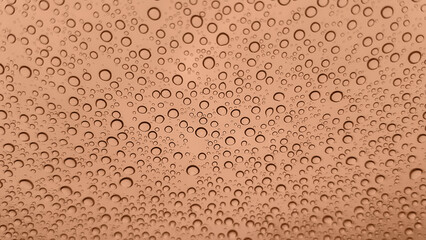 Abstract image of rain drops on glass. Image toned in Peach Fuzz color of the year 2024. New Fashion color. Top view. Abstract drops view.
