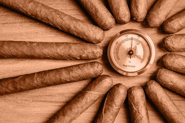 Cigars with humidor hygrometer on the wooden background. Image toned in Peach Fuzz color of the...