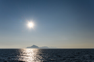 Bright sun, complete with sunburst, in the sky reflecting light across the arctic ocean, mountain...
