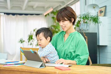 Obraz premium 赤ちゃんを抱えて自宅で仕事をする女性