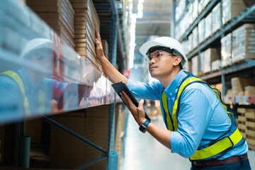 Asian male worker in security suit with tablet computer looking for items in warehouse. Logistics...