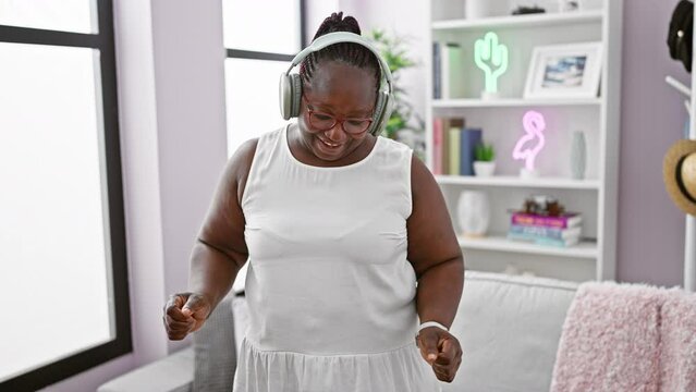 Cheerful african american woman groovin' at home, rocking her braids, confidently enjoying music through her gadget. an expression of joy in her cozy living room, losing herself to the sound