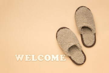 Welcome inscription on a beige background and slippers.