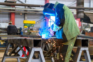 A welder wearing a protective mask for metal welding and protective gloves performs welding work at...